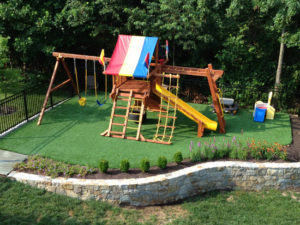 artificial turf backyard with stone retaining wall children's playset with swings & slide