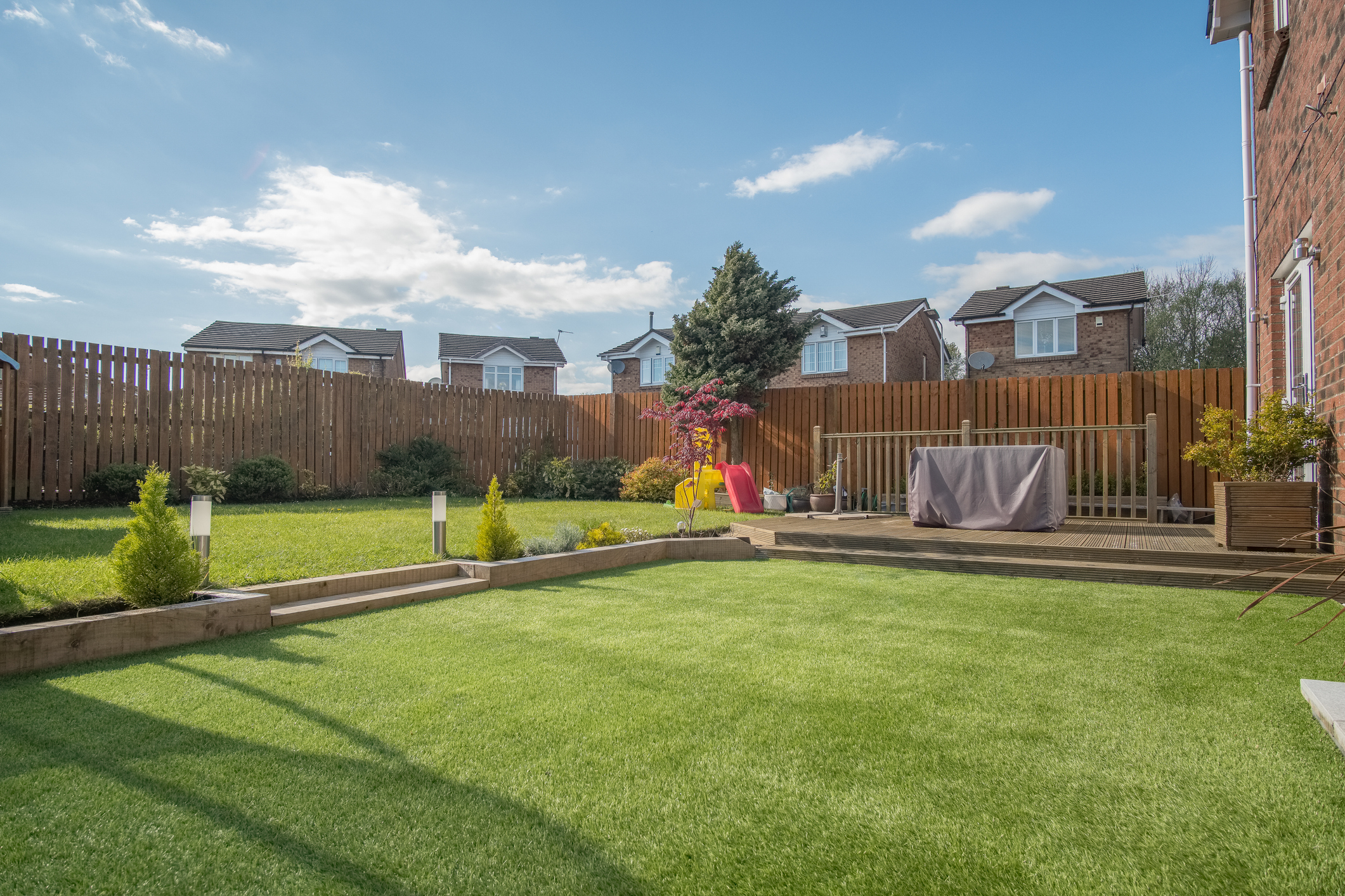 A newly landscaped garden with mix of artificial and natural sown grass and a new decking patio surrounded by new erected wooden fencing and modern homes for is-artificial-turf-worth-it-for-rental-properties blog.