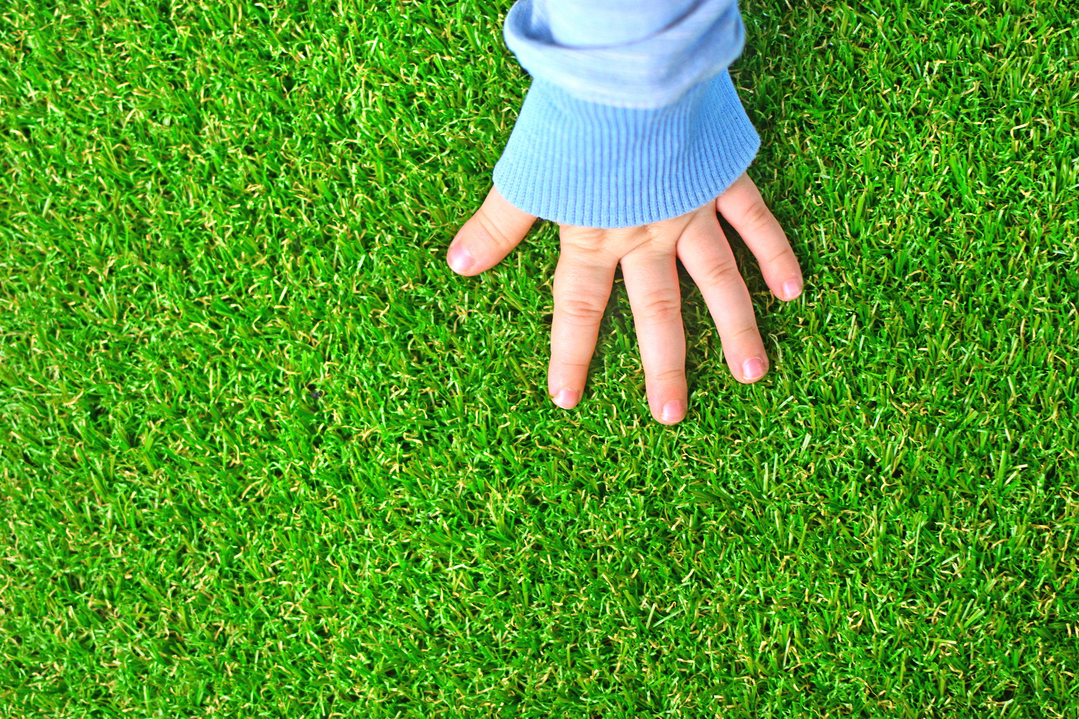 The hand of a baby on a green artificial turf floor for is-artificial-turf-safe-for-kids-and-pets blog.