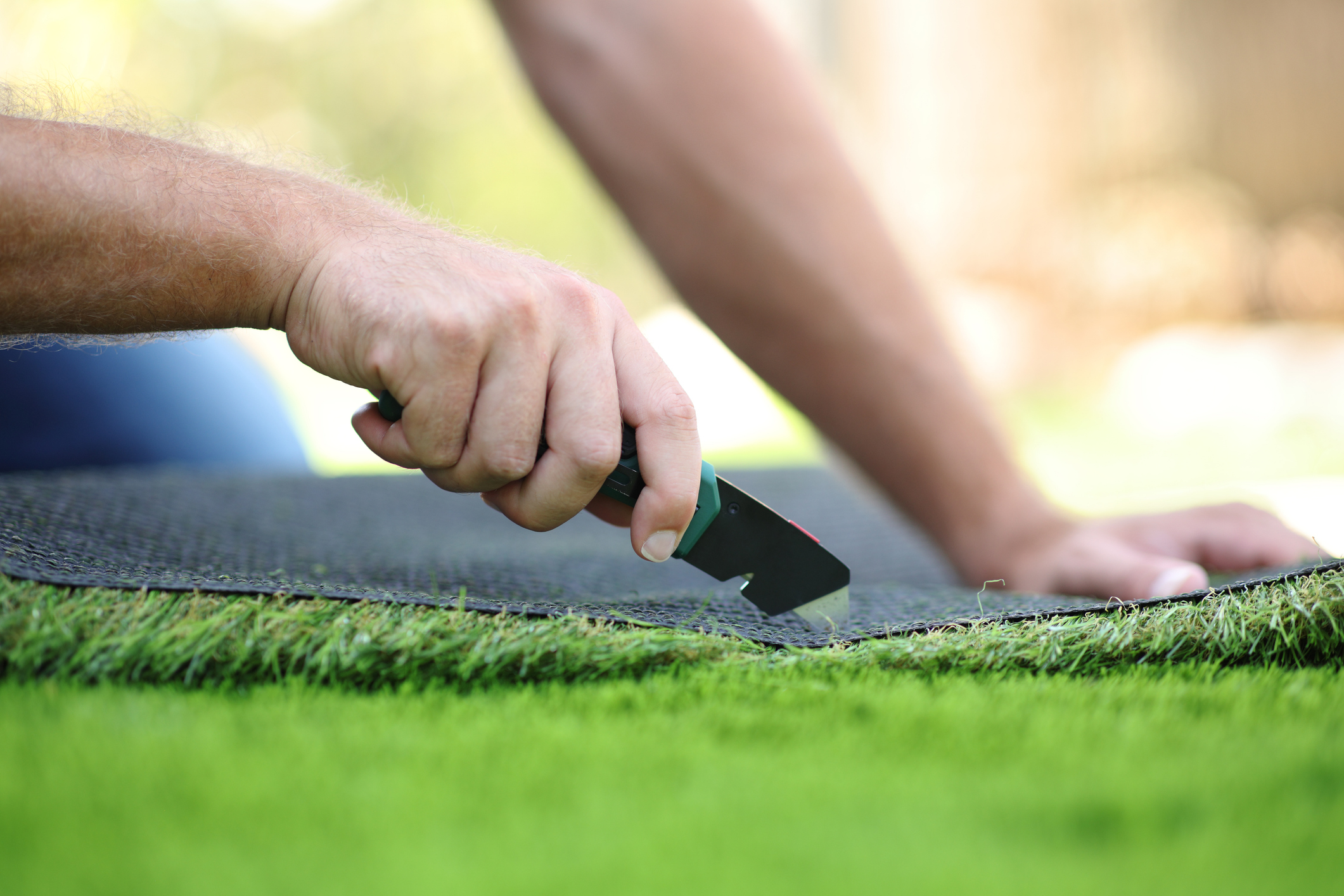 Close up of a man's hand cutting and installing artificial grass for high-quality-turf-installation blog.